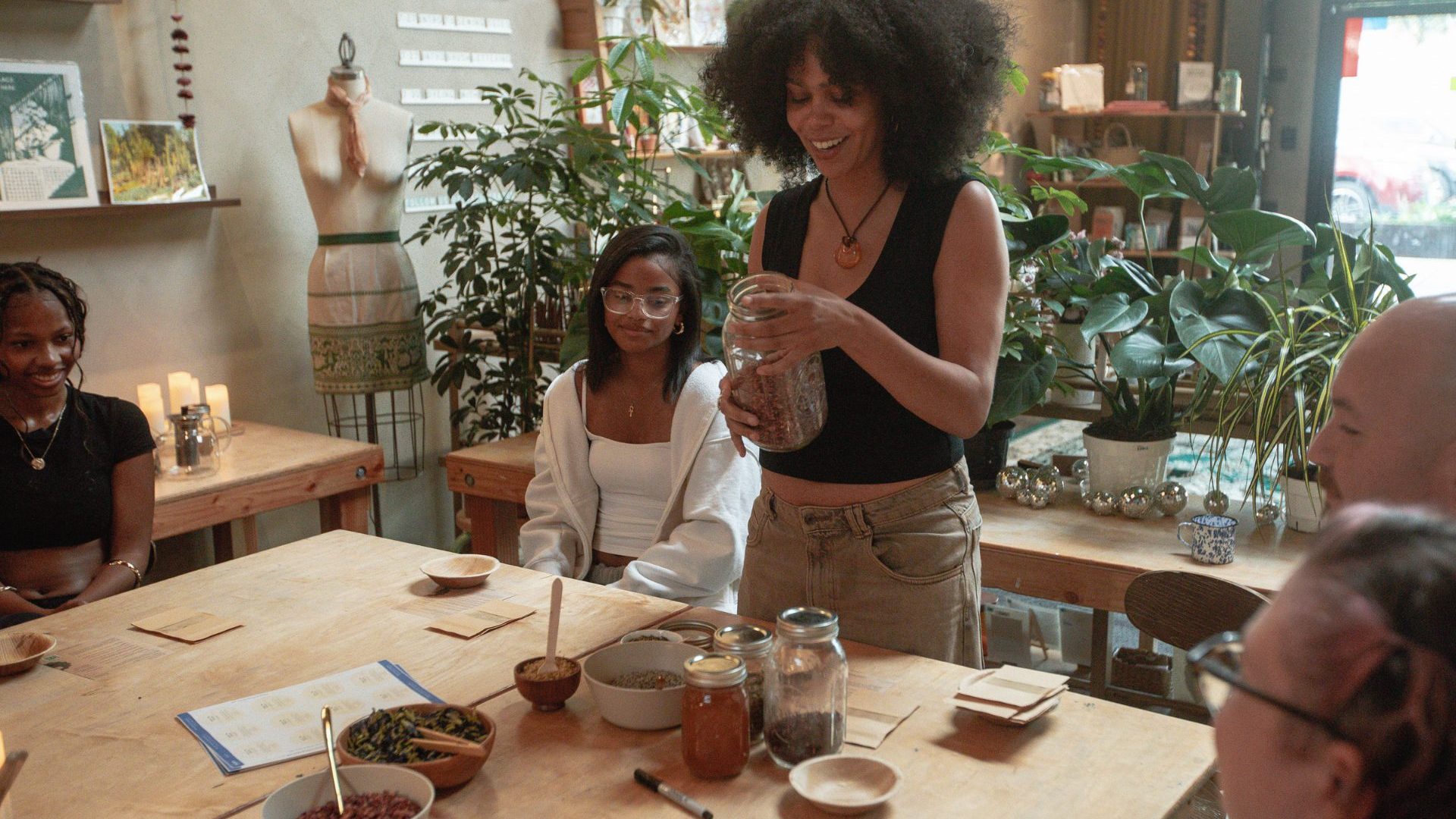 Woman stands by table demonstrating how to mix dried leaves to make your own tea blend.
