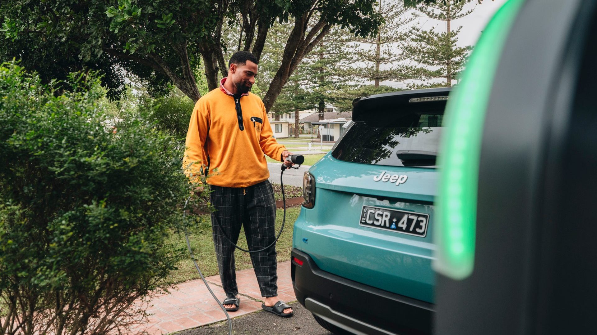 Man wearing orange sweater charges blue electric vehicle