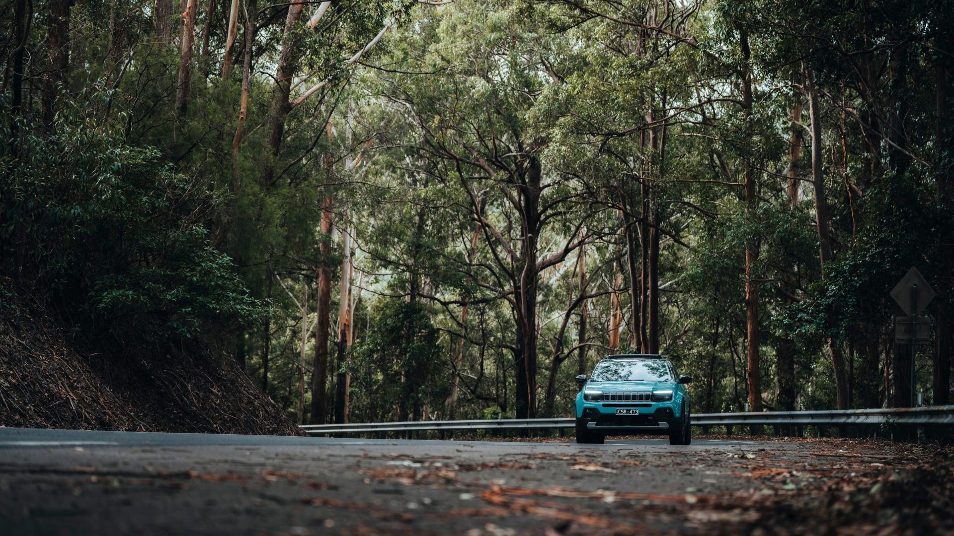 Blue electric vehicle drives through green forest
