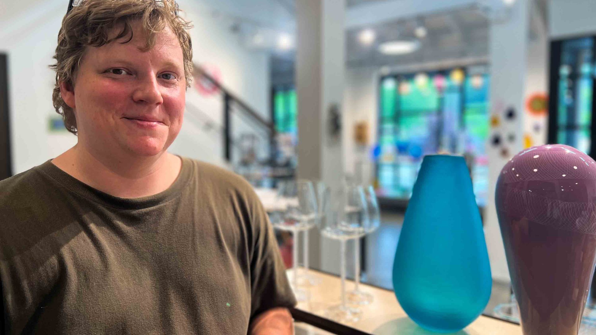 A glass artist smiles to camera beside contemporary glass designs