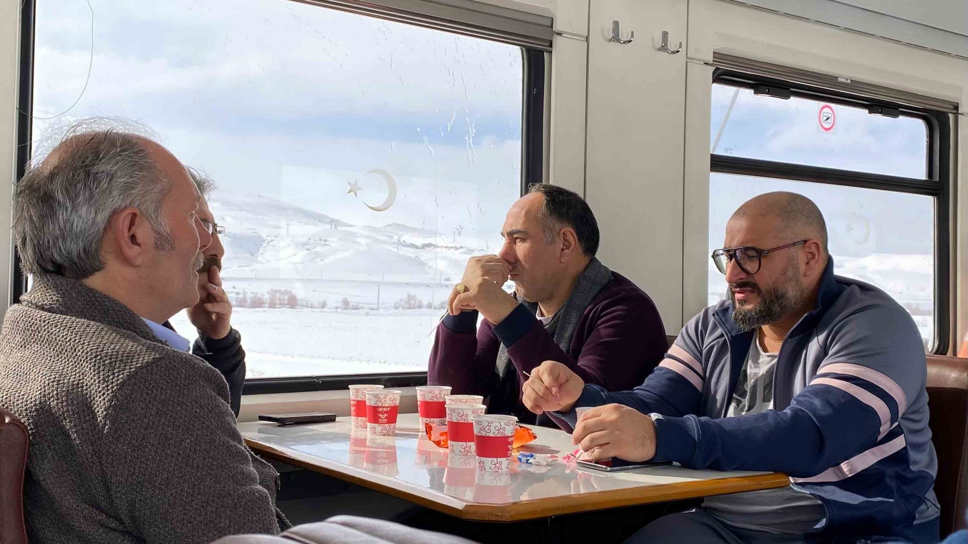 Three men sit together and talk while drinking coffee.