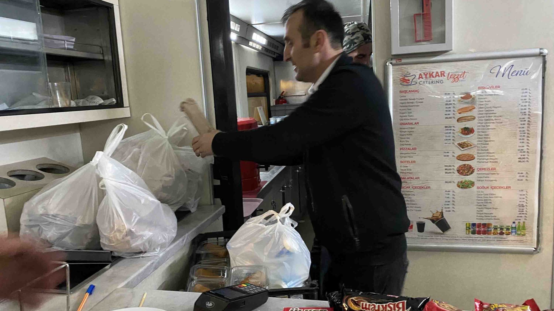 A man is packing bags of food in the train's dining car.