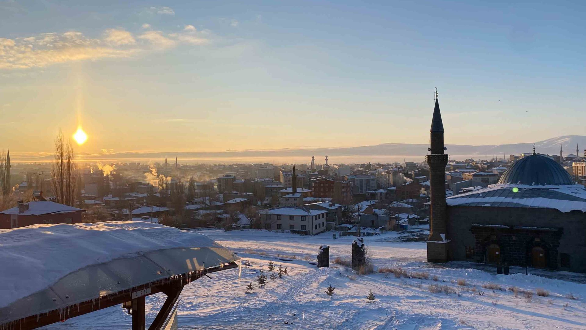 A snowy cityscape at sunset, with a minaret in the foreground.