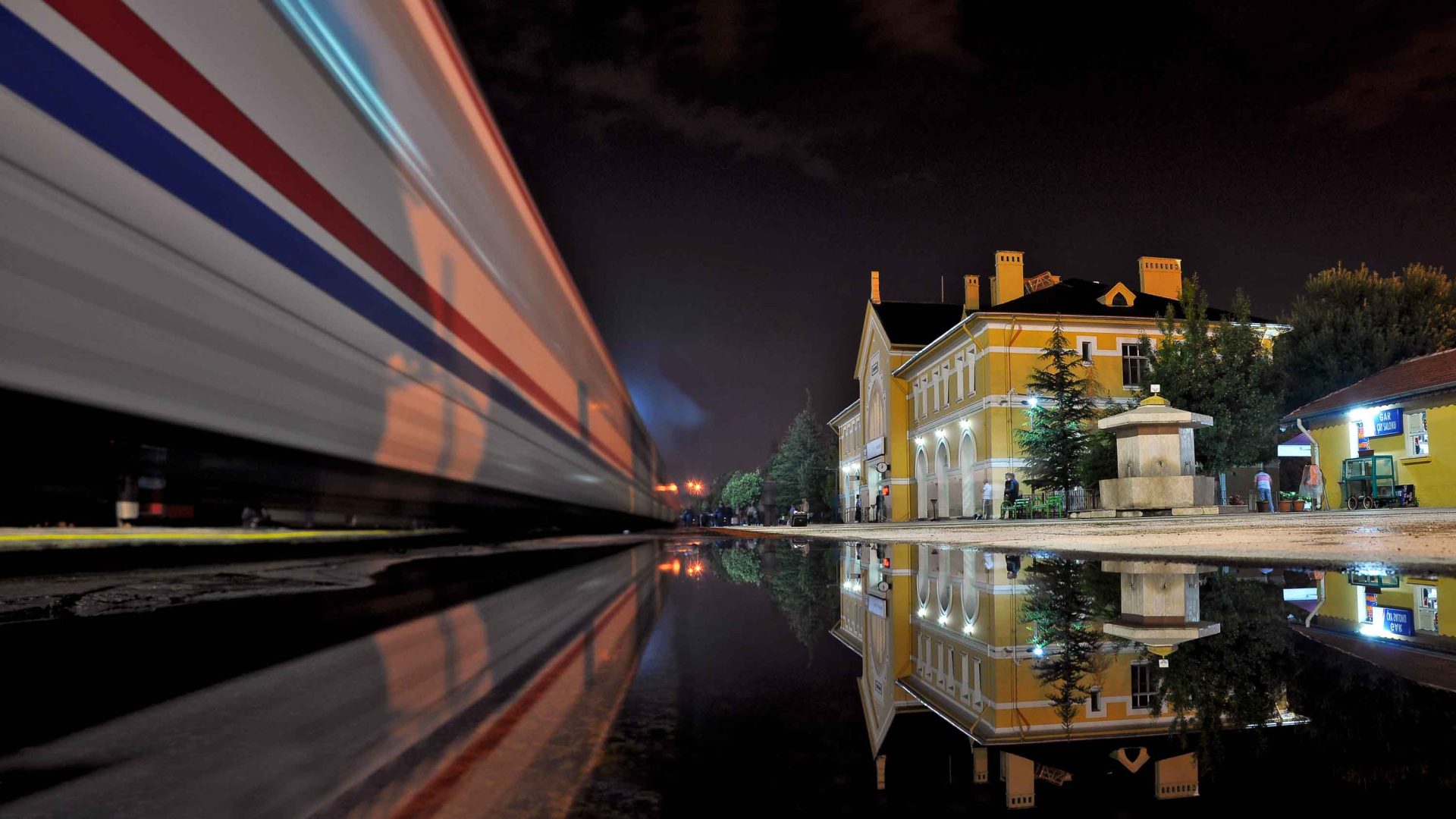 A train speeds past a yellow building.