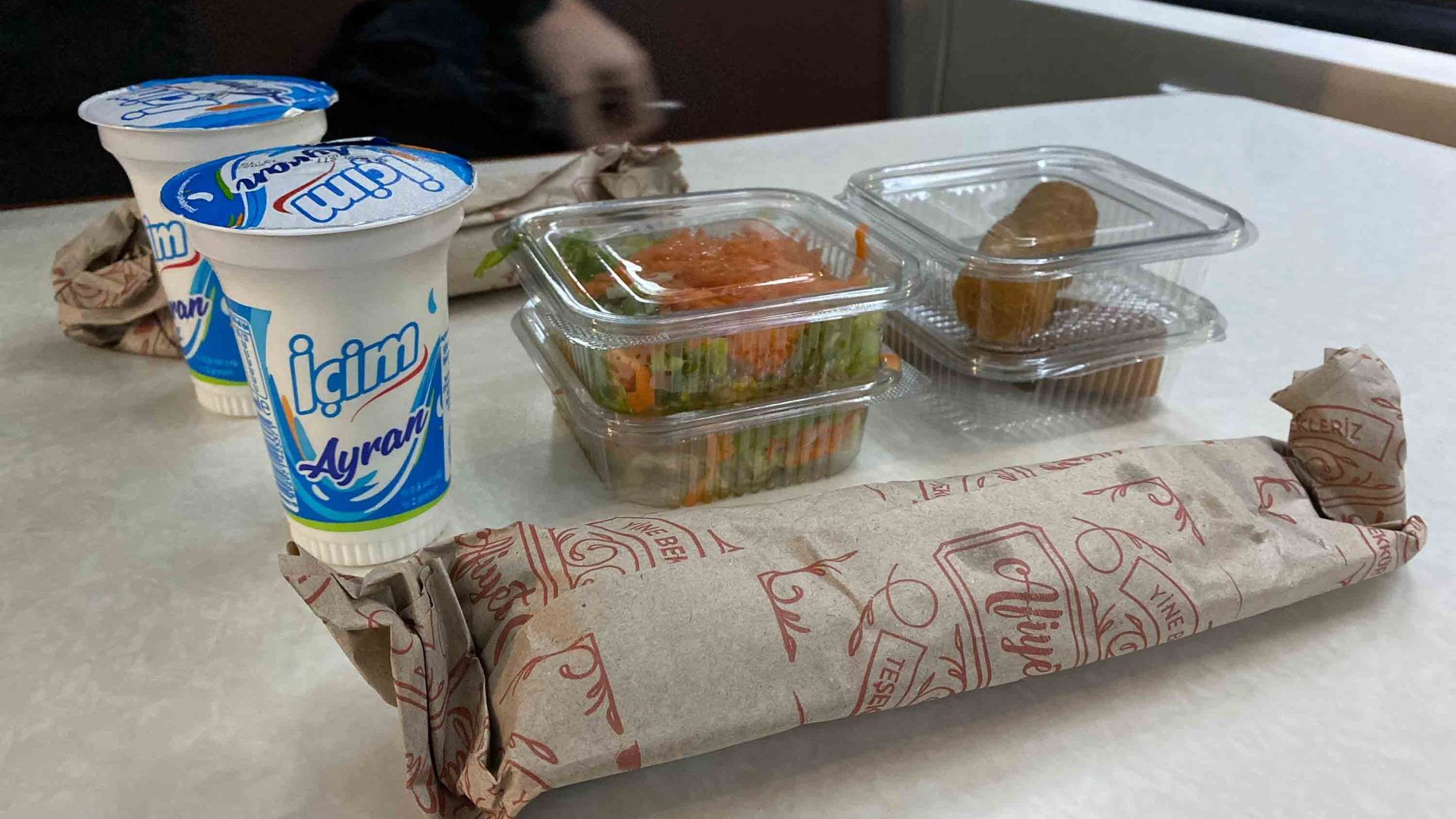 A kebab, salad and yoghurt drinks on a table.