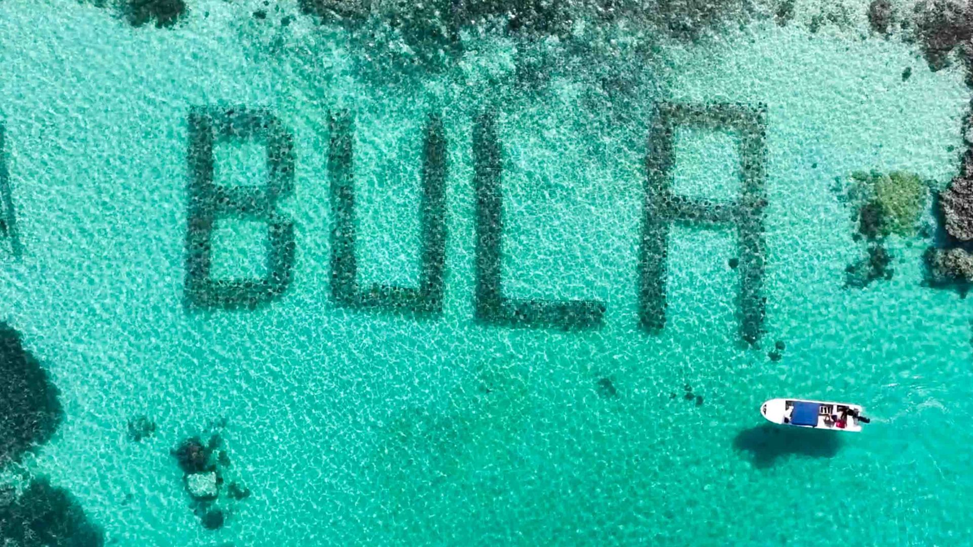 A boat passes the coral conservation structure that spells out the word 'Bula'.