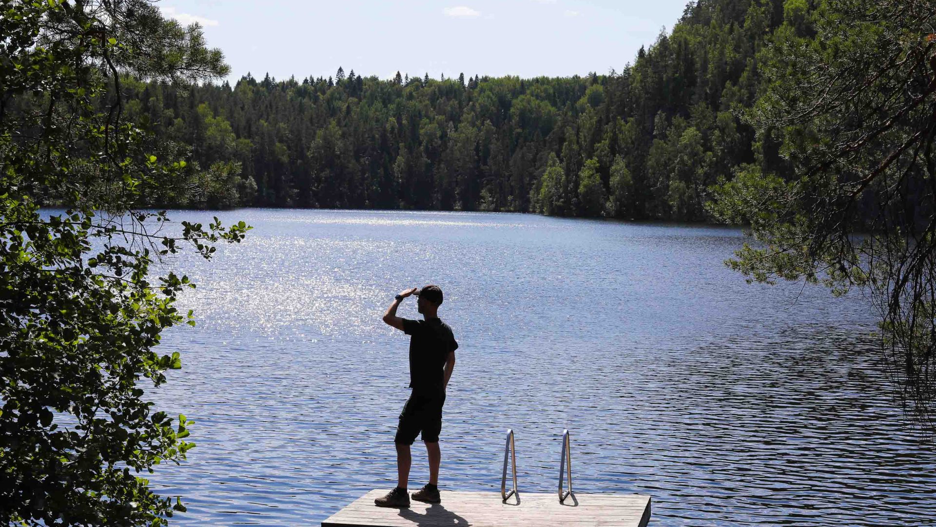 A man stands and looks out at a lake from a rock.