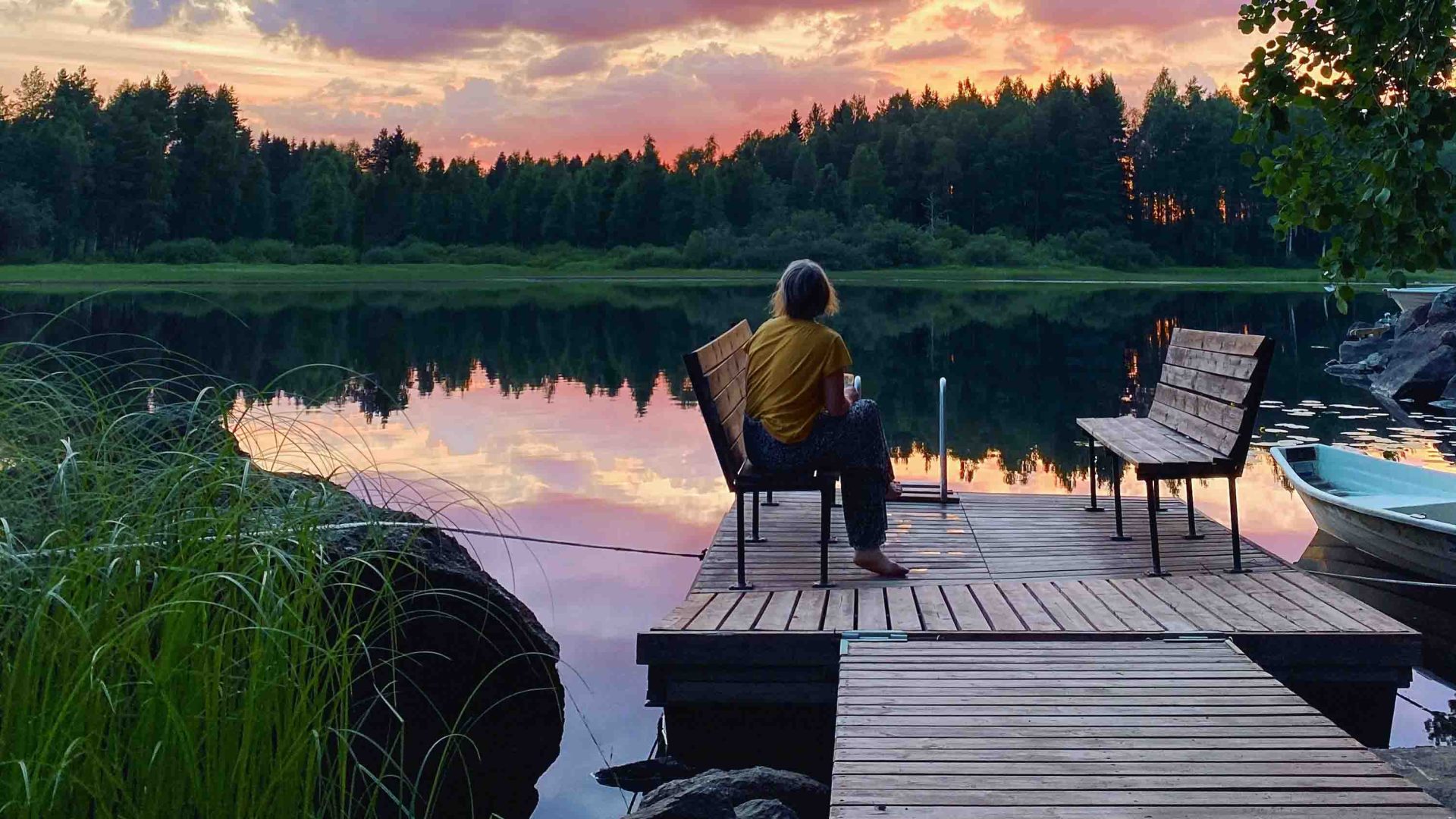 A woman sits and enjoys a lake view at the end of a day.
