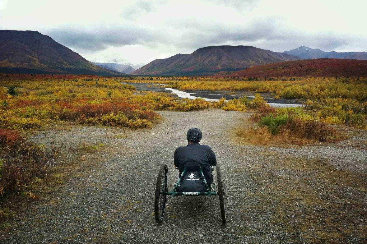 A man in a handcycle looks toward some mountains.