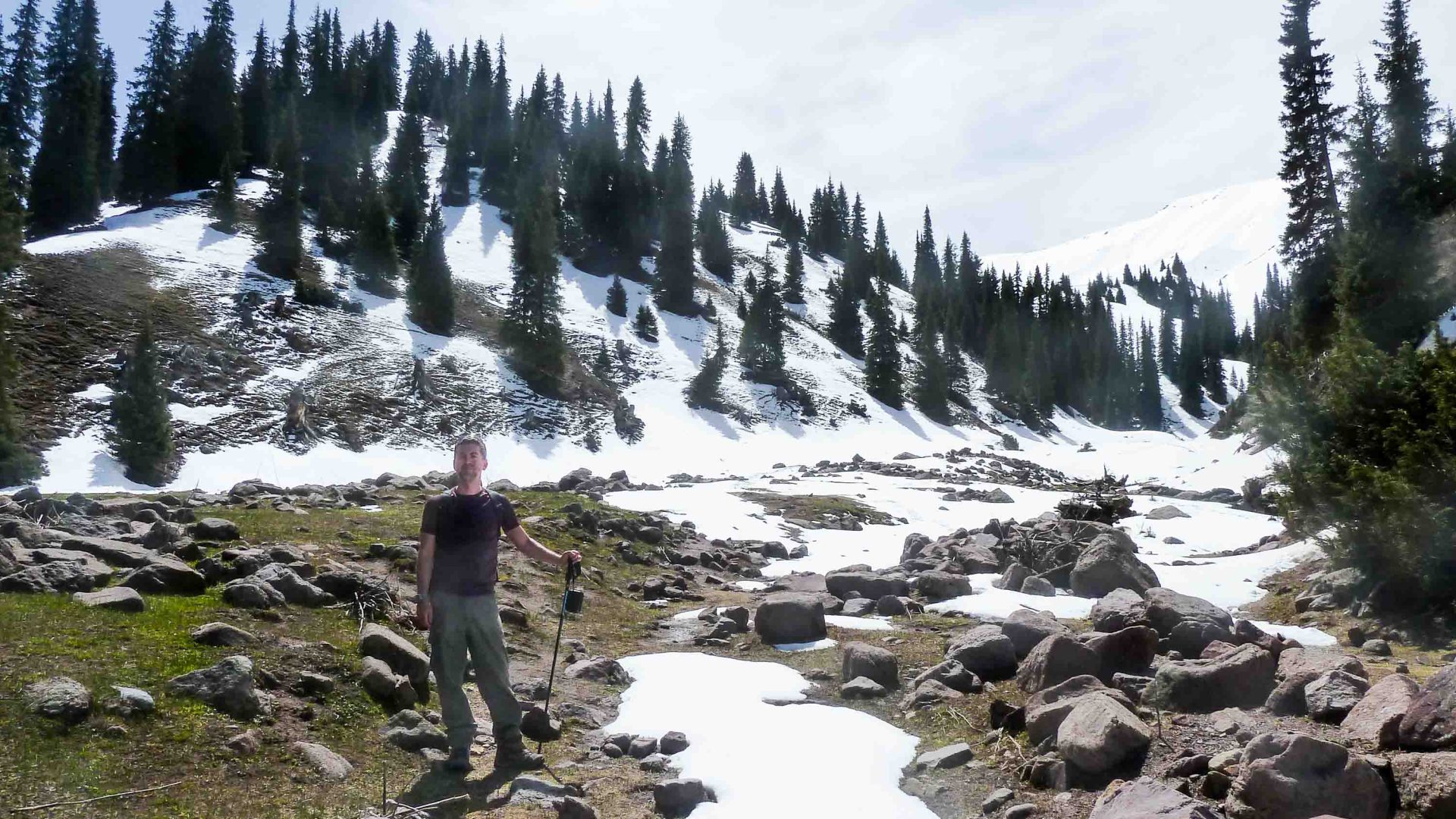 A man stands in the snow with mountains behind him.