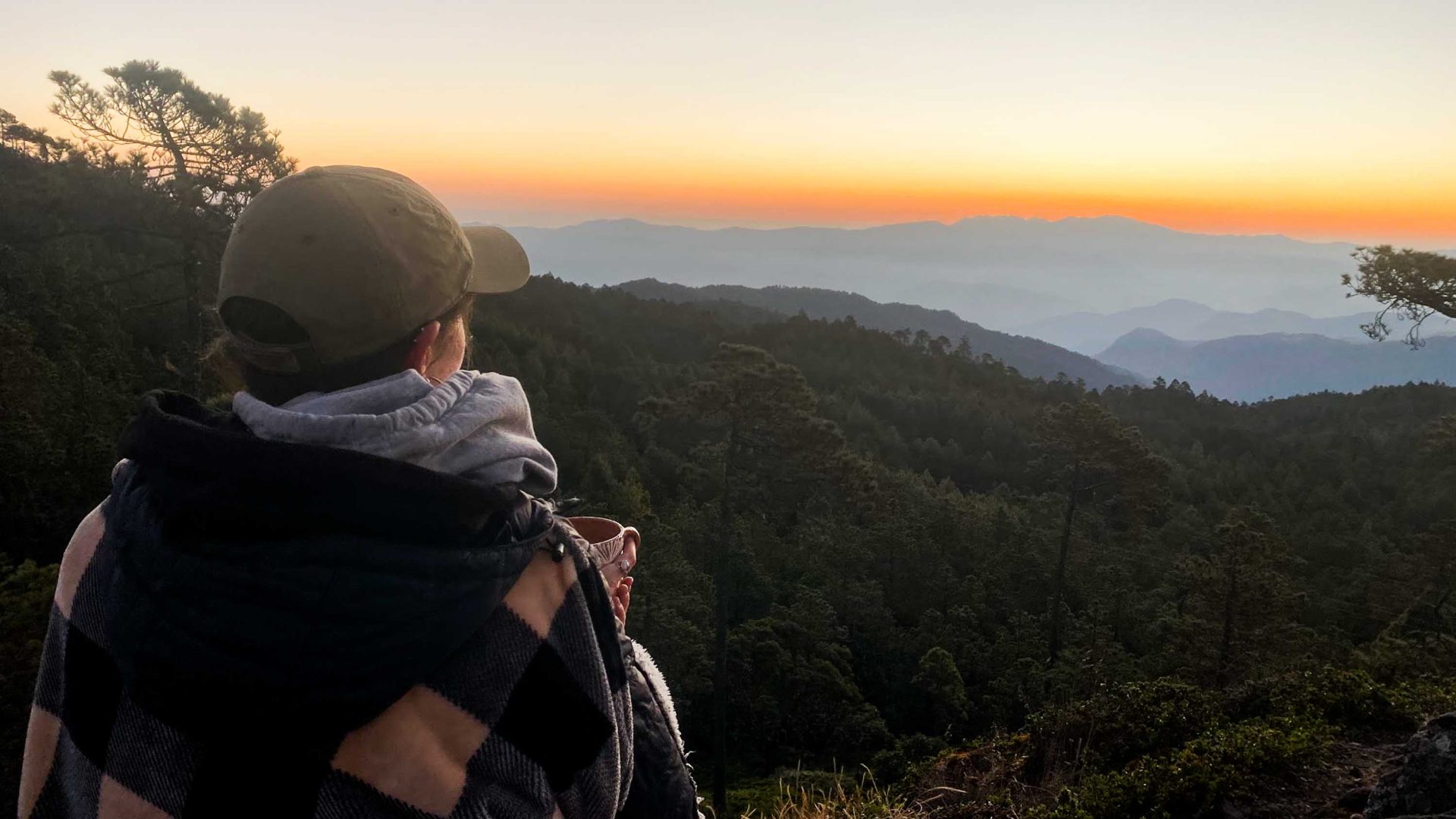A woman looks out at a sunset over a valley.