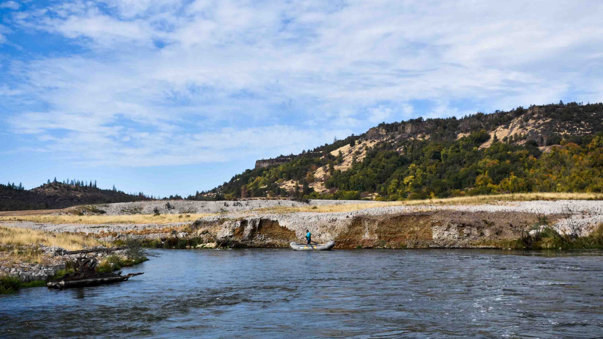 person stands up in a raft alongside the shore in one of the calmer part of the river.