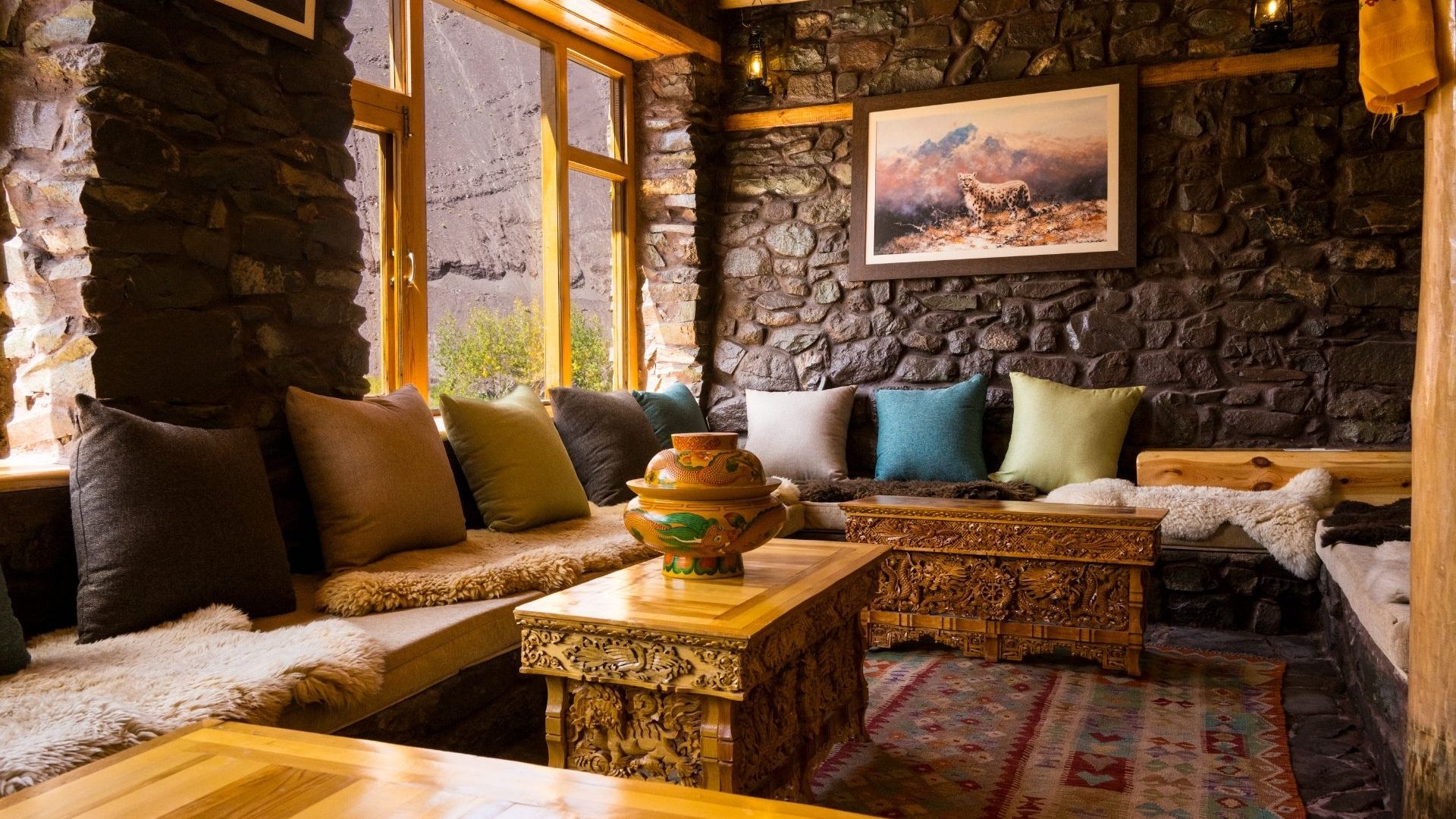 A cosy communal lounge with stone walls, ornate furniture, big cushions and a decorated rug