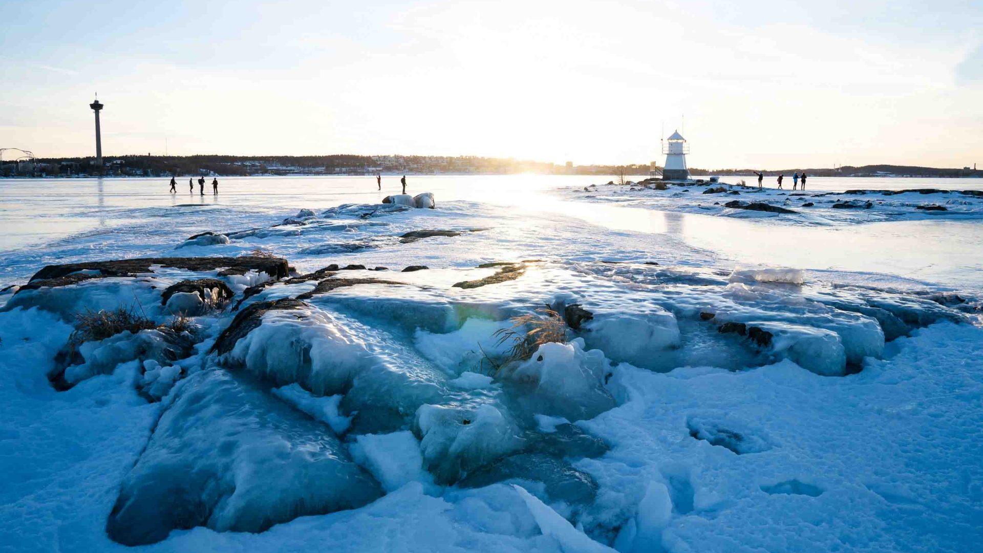 An ice covered lake with a lighthouse in the background.