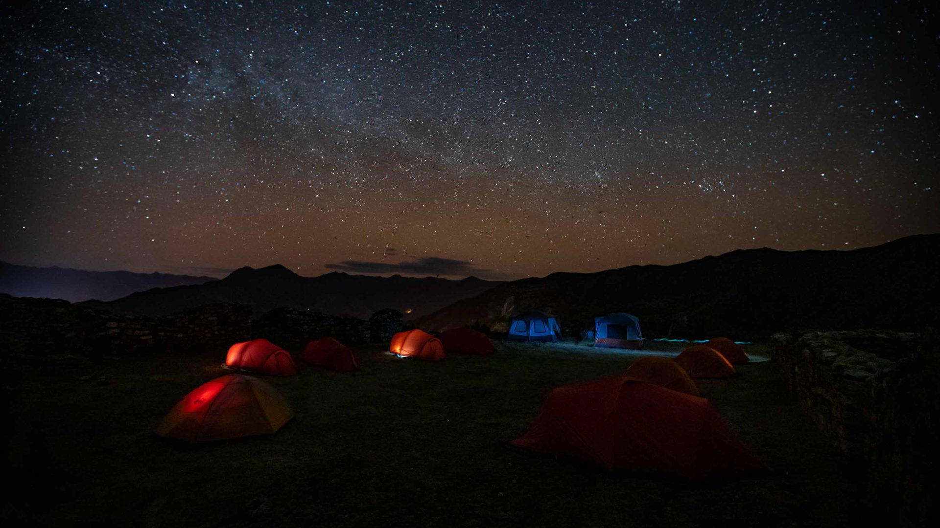 Tents are lit up under a starry sky.
