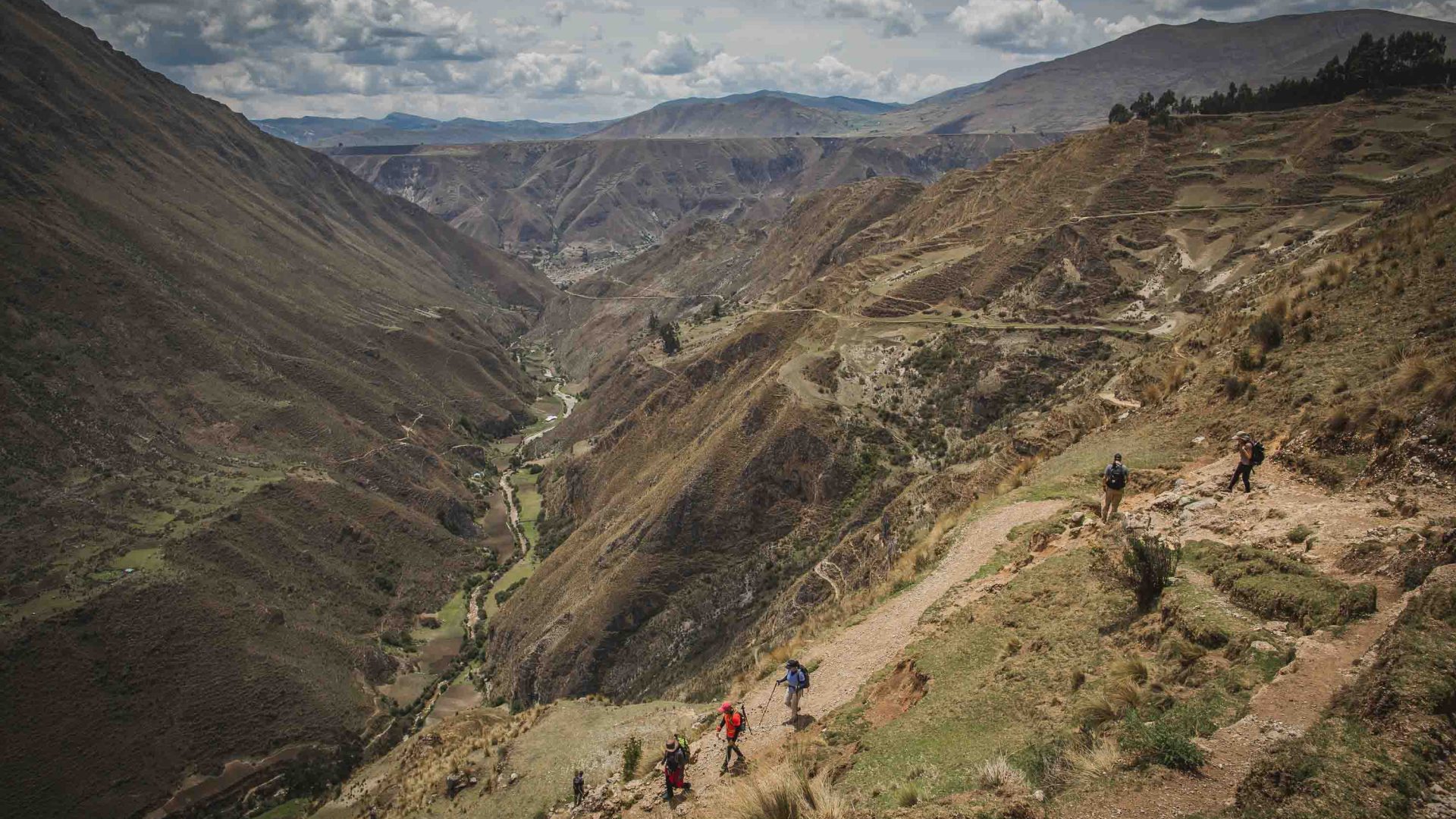 People hike along a path that drops to a valley.