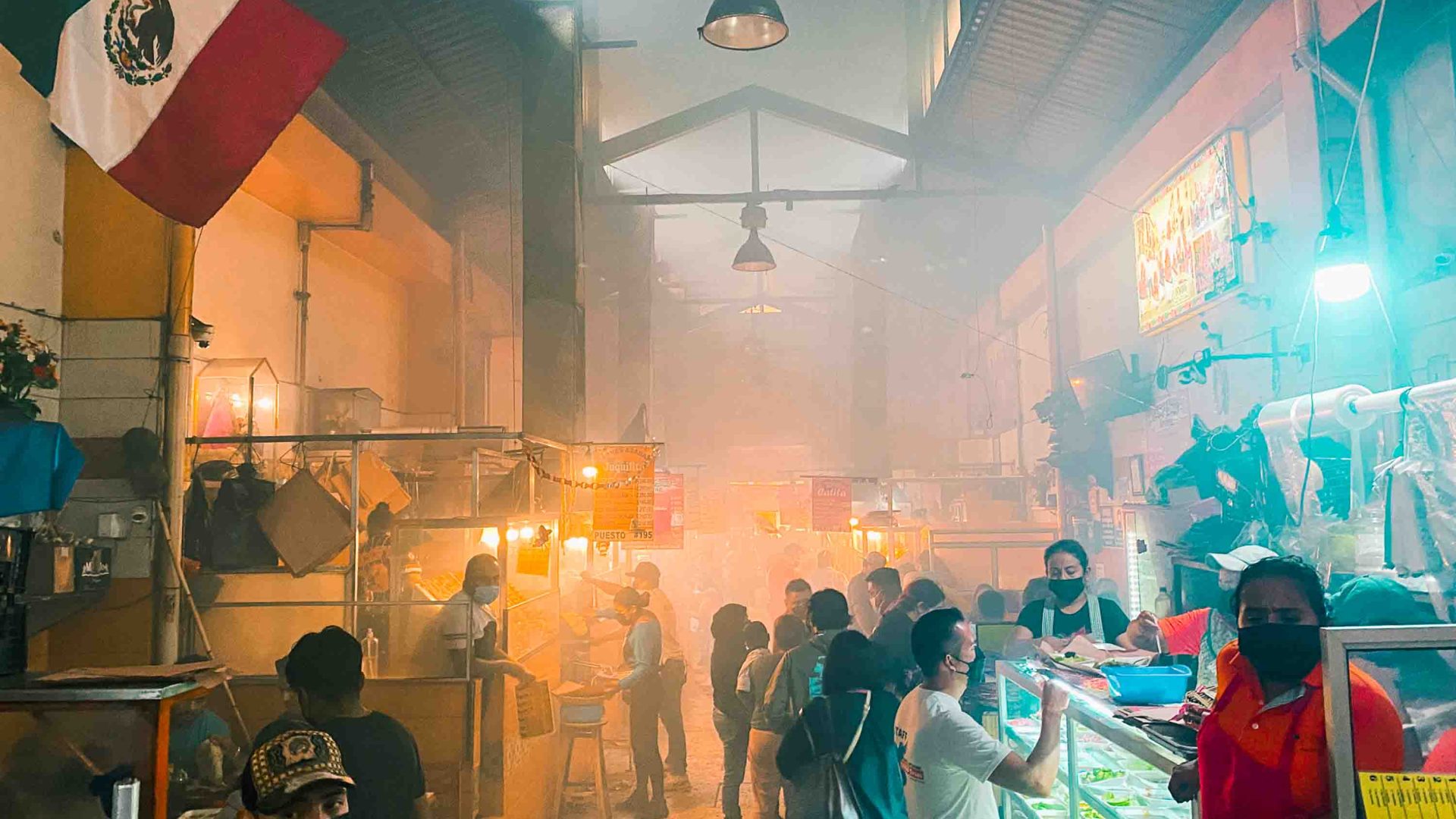 A smoky market scene with vendors and people eating and standing around.