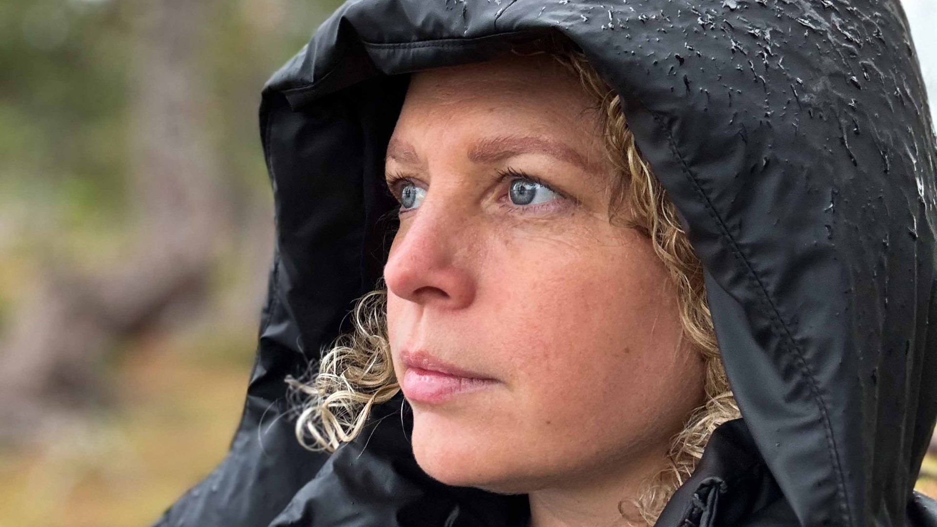 A woman in a black hooded rain jacket looks away.