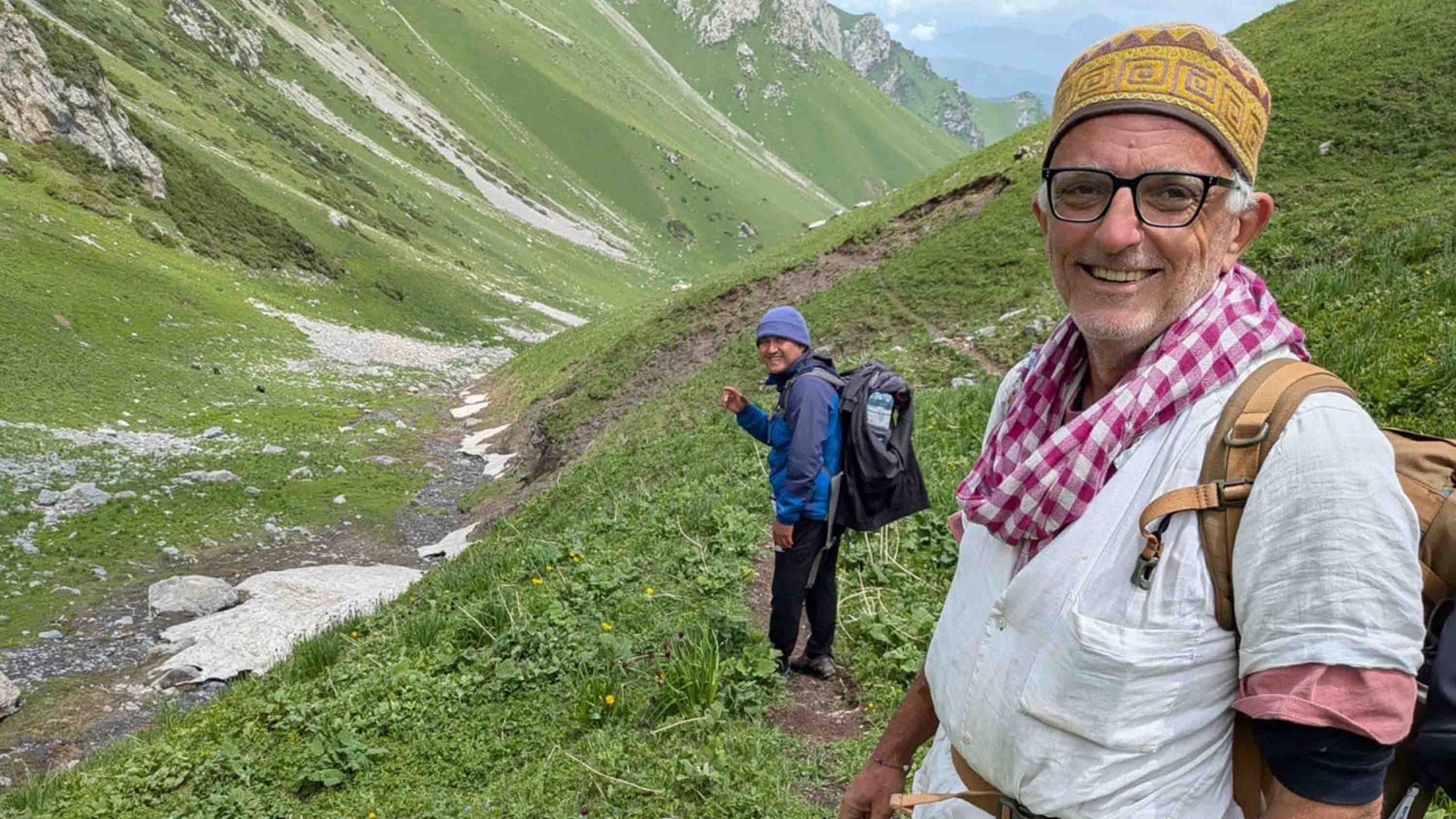 A man smiles on a mountain with his guide in the background.
