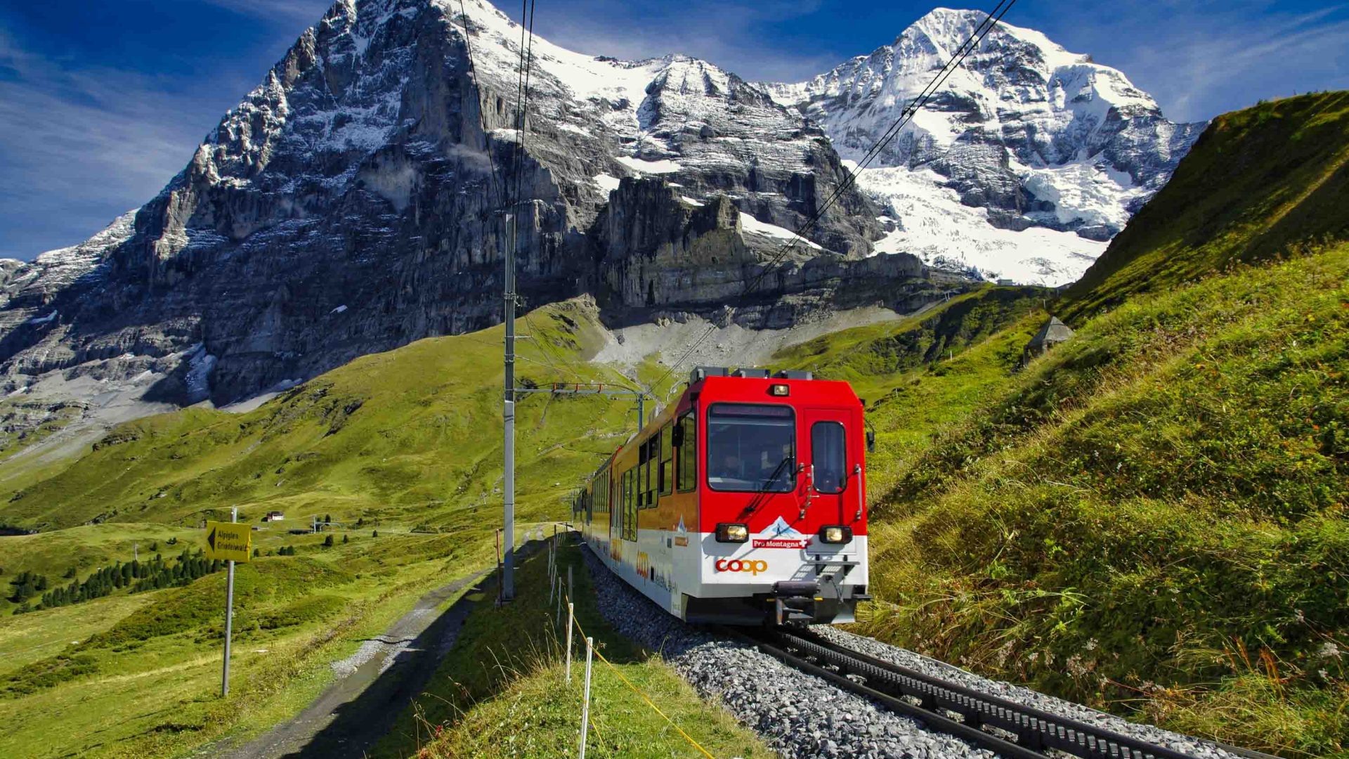 A red train passes under the mountains of the Swiss Alps.