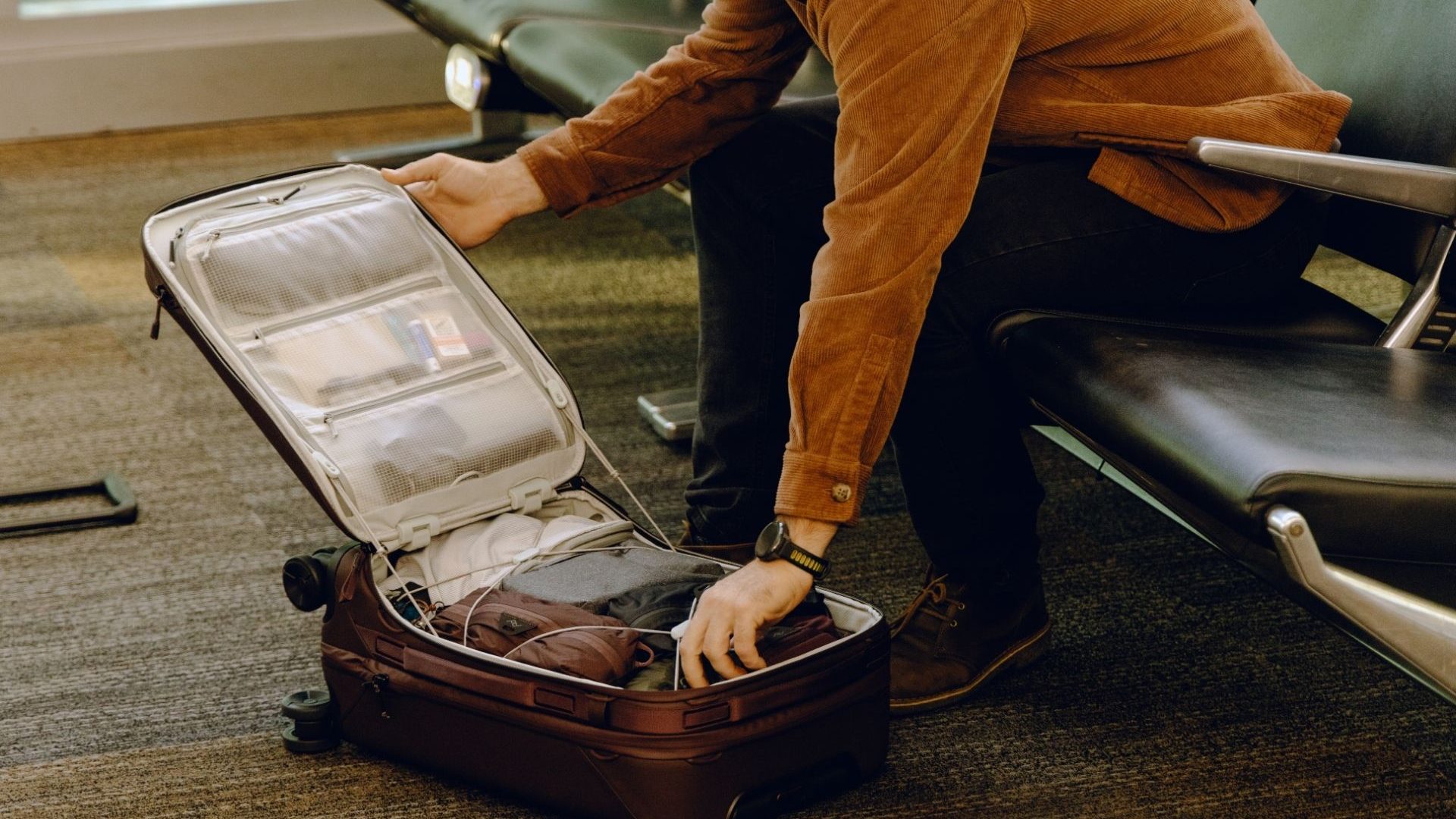 A traveler sits at an airport gate and opens their suitcase.